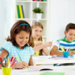 Portrait of lovely girl drawing at workplace with schoolmates on background
